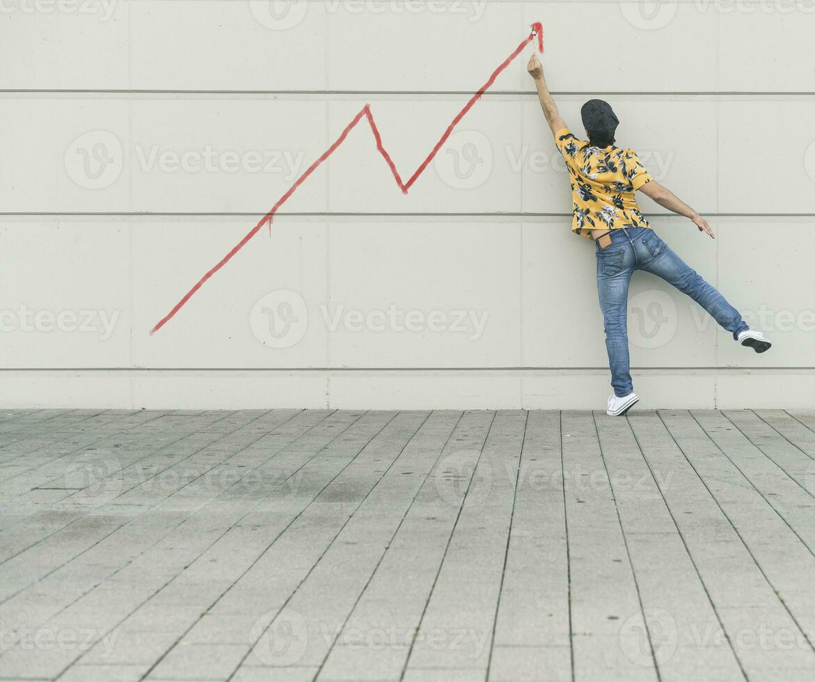 Digital composite of young man drawing a line graph at a wall photo