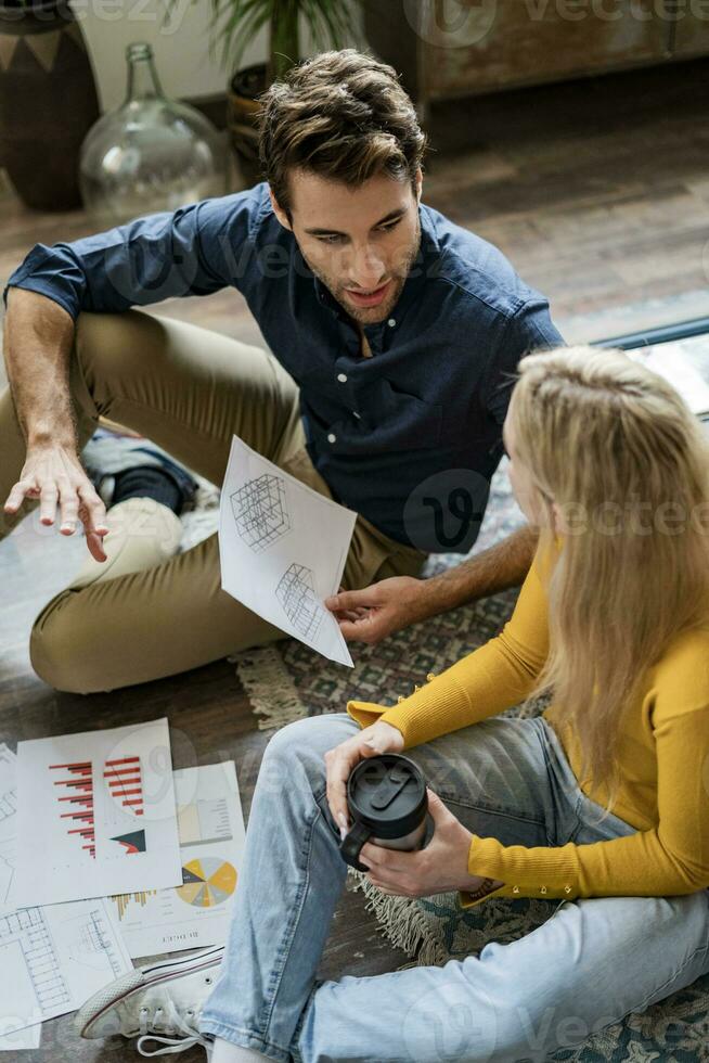 Businessman and businesswoman sitting on the floor discussing documents in loft office photo