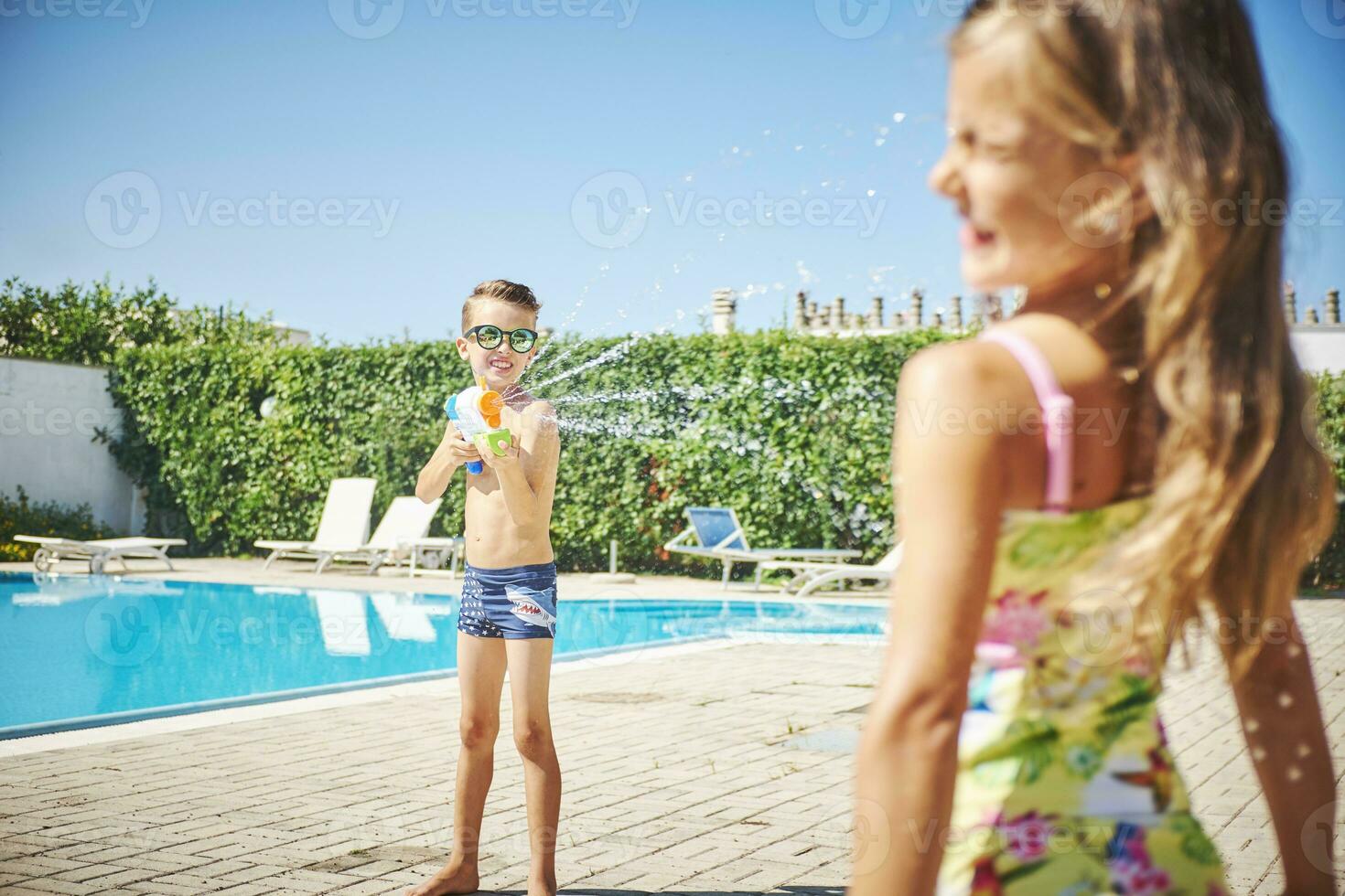 Boy with water gun splashing at girl at the poolside photo