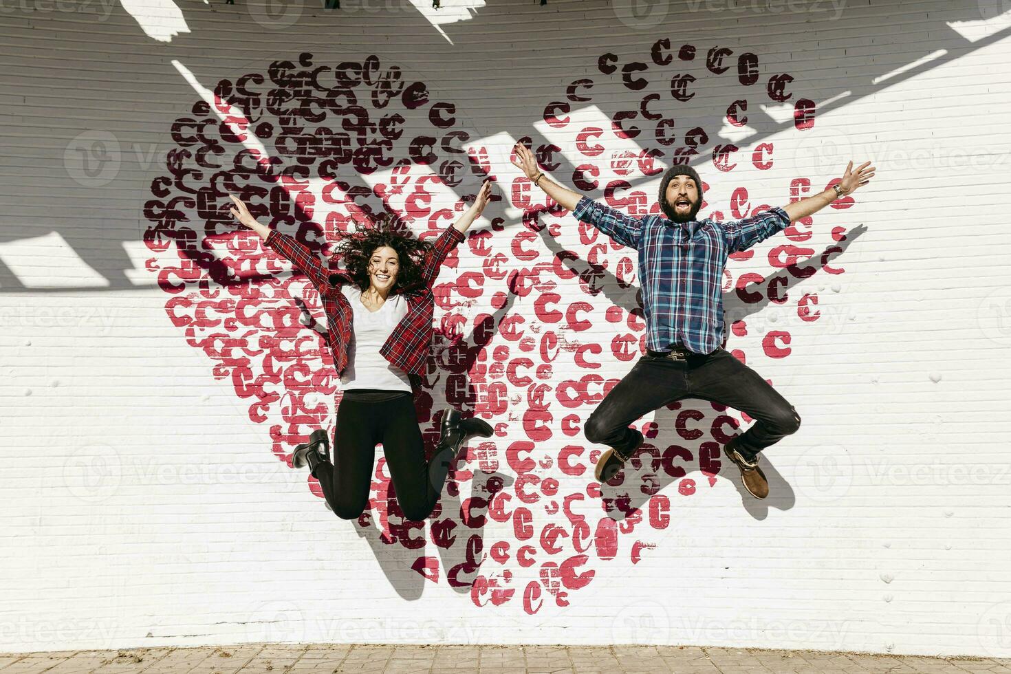 Happy young couple jumping in front of a brick wall with a heart photo