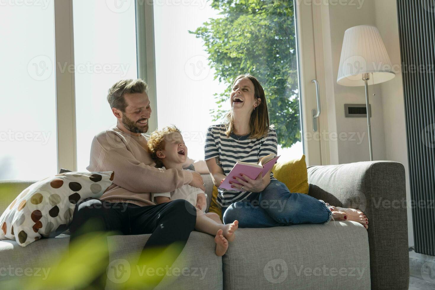 Cheerful family enjoying reading story book while sitting on sofa at home photo