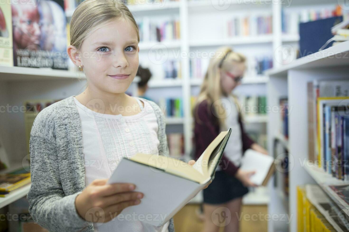 Portrait of smiling schoolgirl with book in school library photo