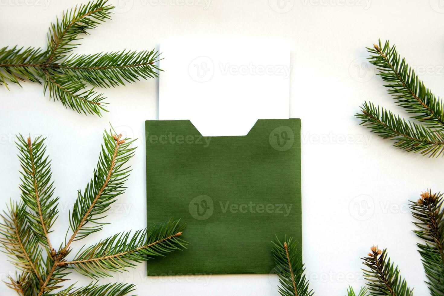 Layout of a stylish Christmas card. Green envelope on a white background with a frame of spruce branches. Christmas Eve. photo