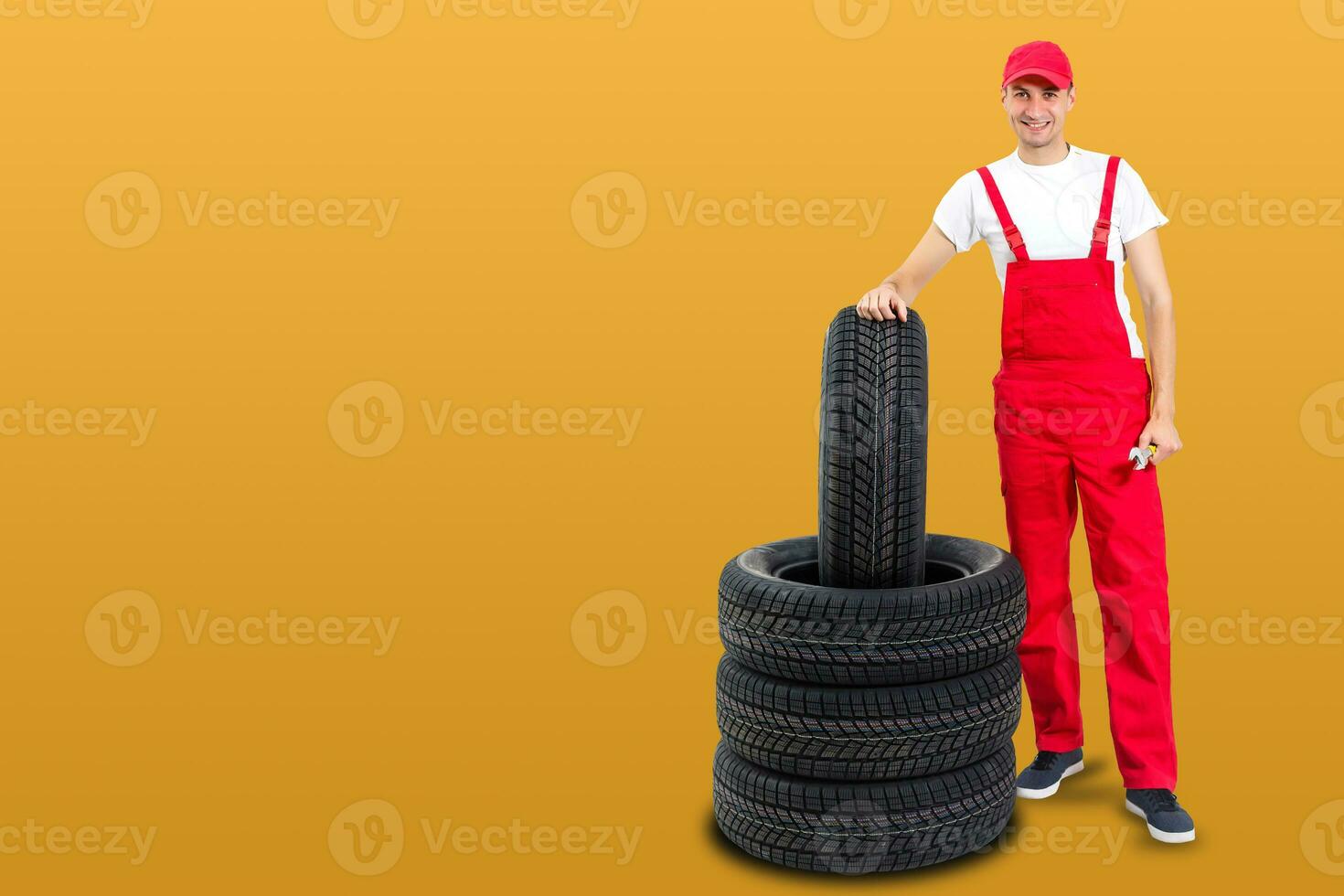 car mechanic carrying tire on yellow background. happy man smiling amd looking into camera photo