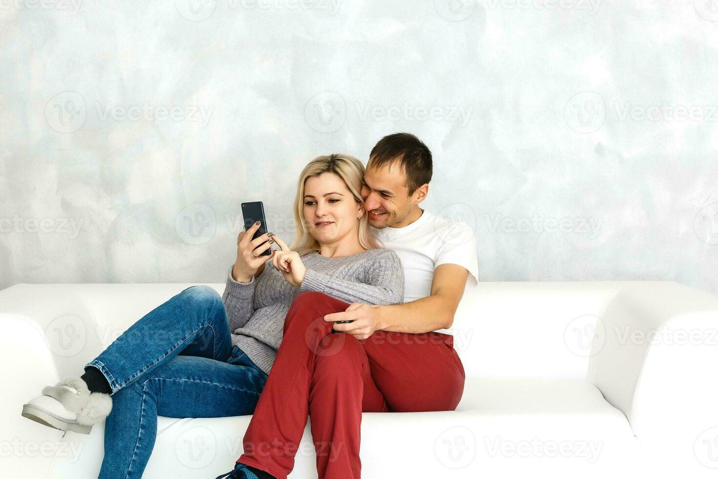 Happy couple enjoying media content in a smart phone sitting on a couch at home photo