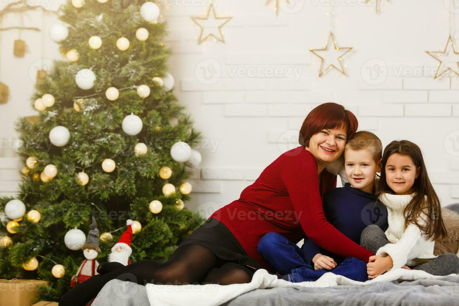 Family on Christmas eve at fireplace. Mother and little kids opening Xmas presents. Children with gift boxes. Living room with traditional fire place and decorated tree. Cozy winter evening at home. photo