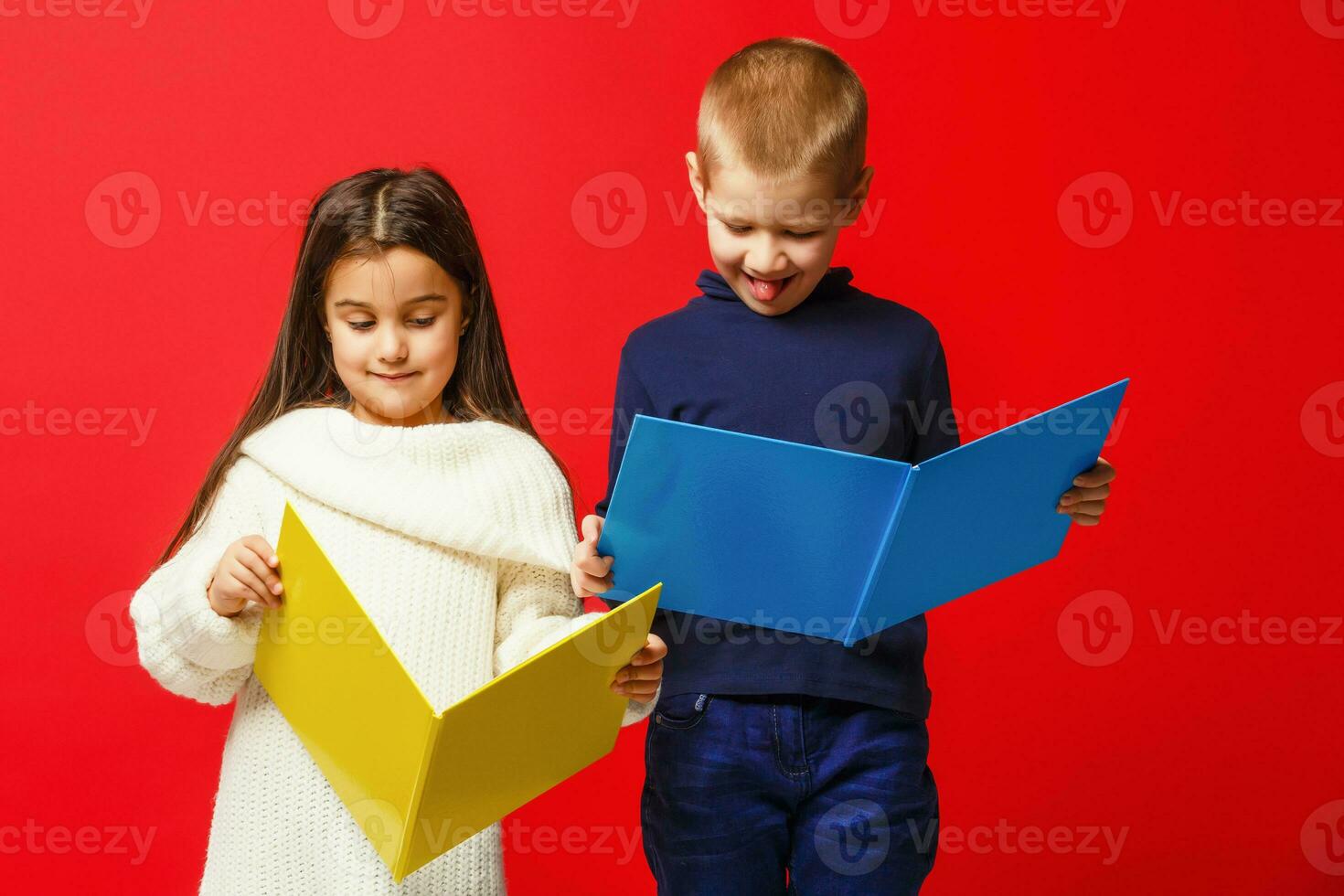 Two smiling school kids with colorful stationery, isolated on red background. School, education concept. photo