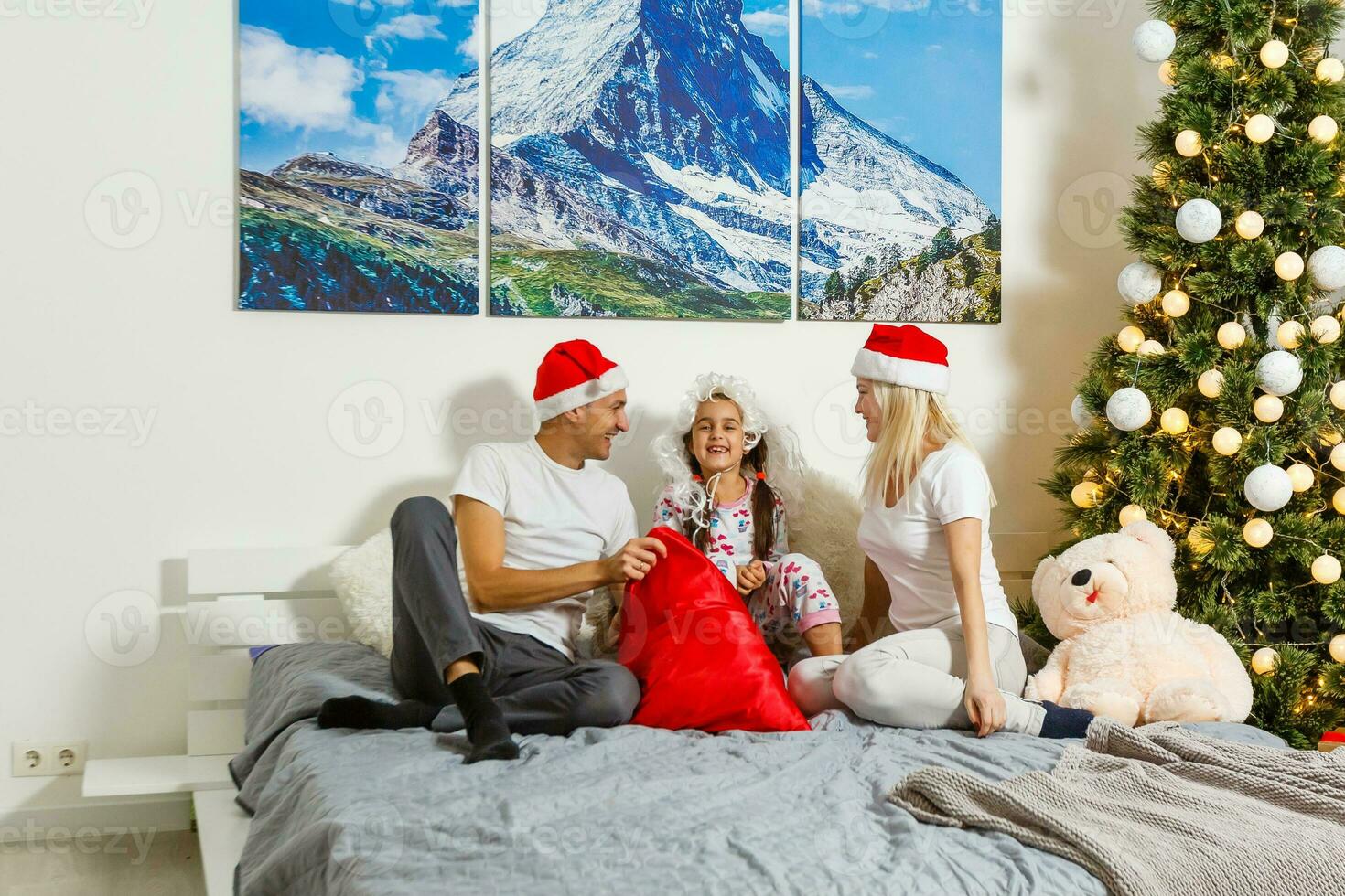 contento familia a hogar. madre, padre y niño acostado en el cama con Navidad regalo. invierno fiesta concepto foto