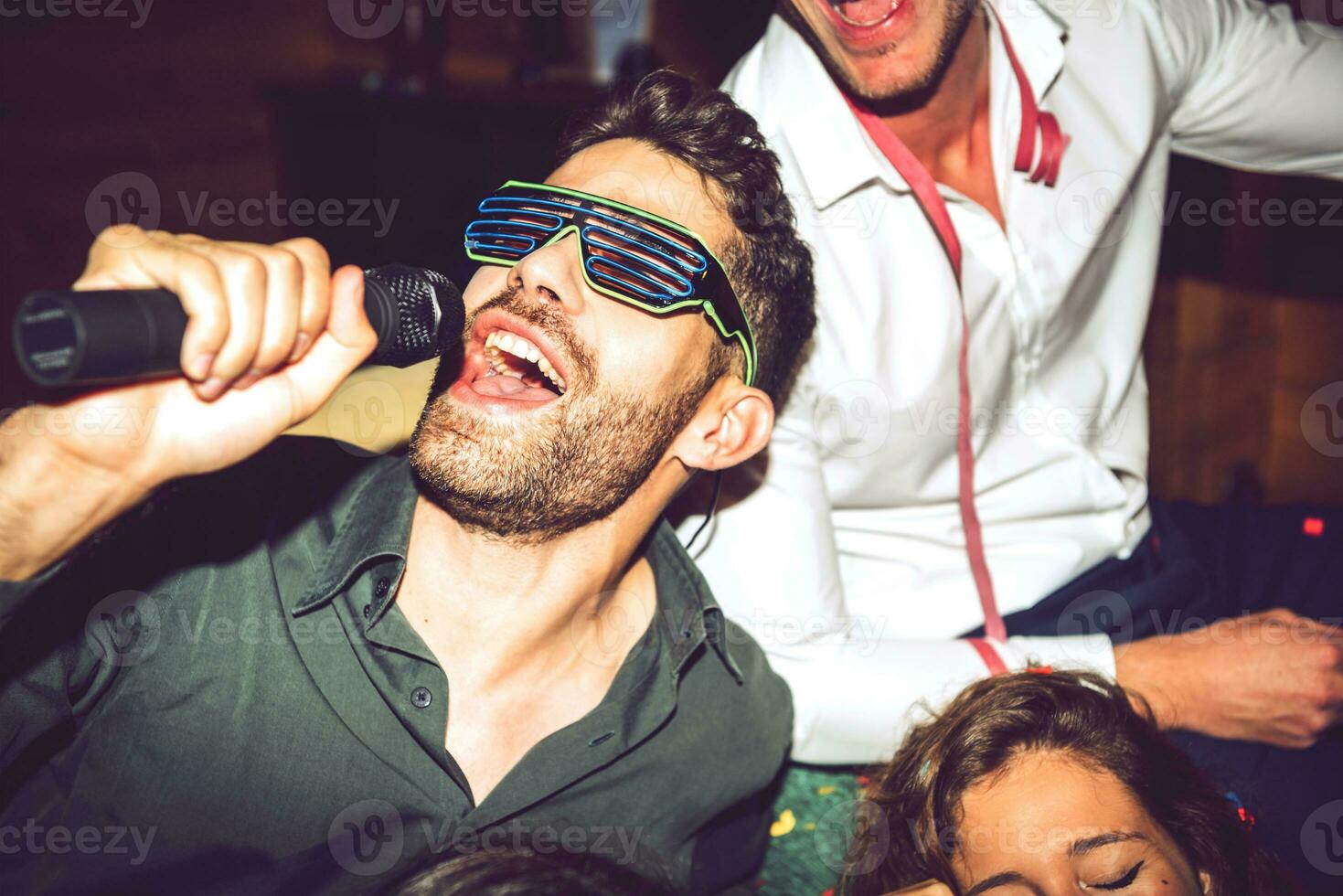 Close-up of young man singing karaoke while enjoying with friends in party photo