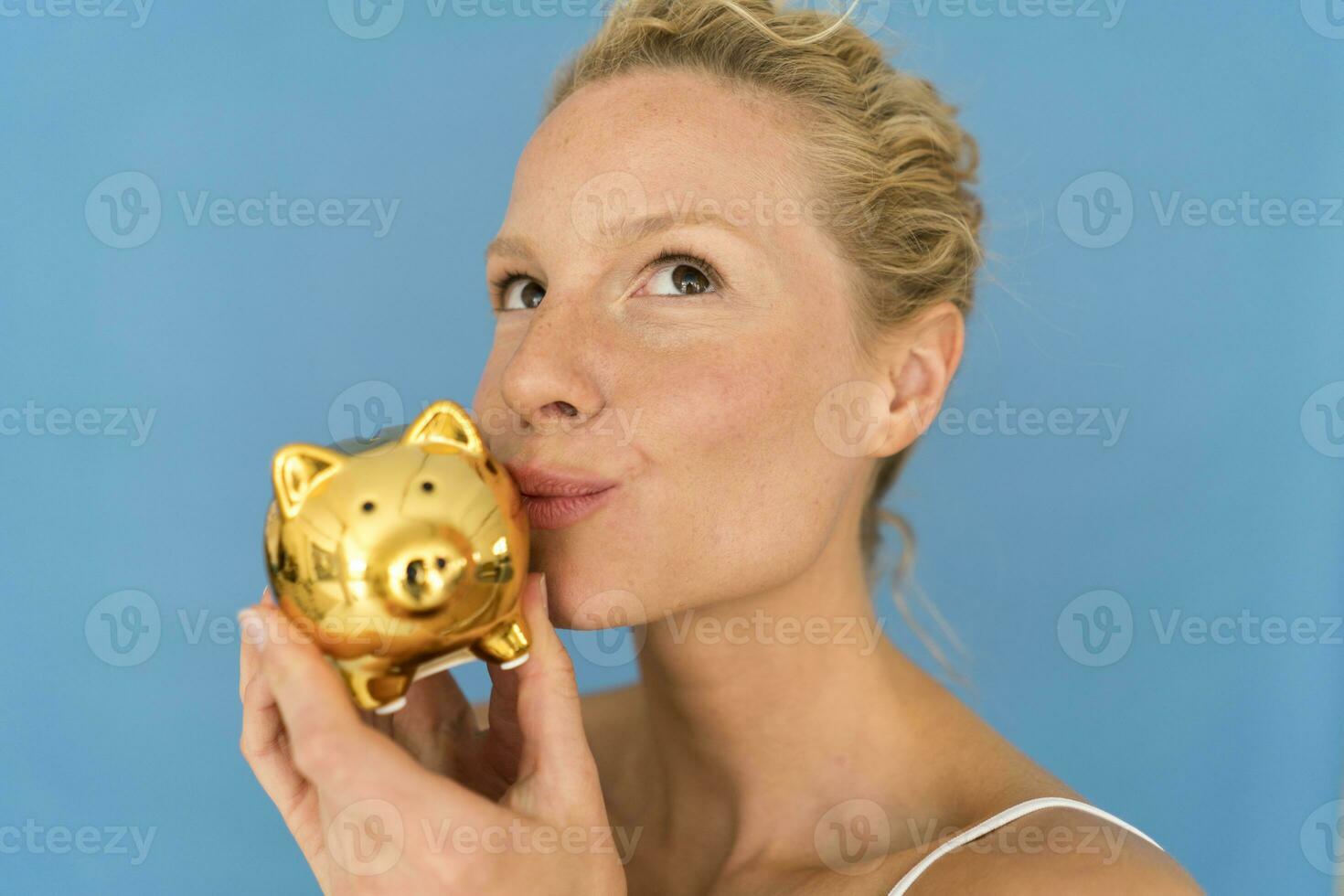 Portrait of blond woman kissing golden piggy bank photo