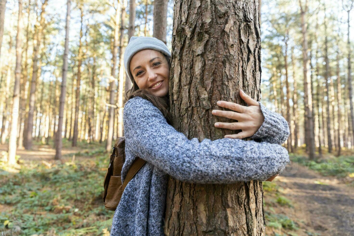 sonriente hembra caminante abrazando árbol maletero mientras explorador en cannock persecución bosque foto