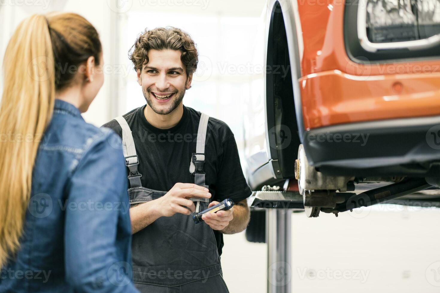 Happy car mechanic talking to client in workshop photo