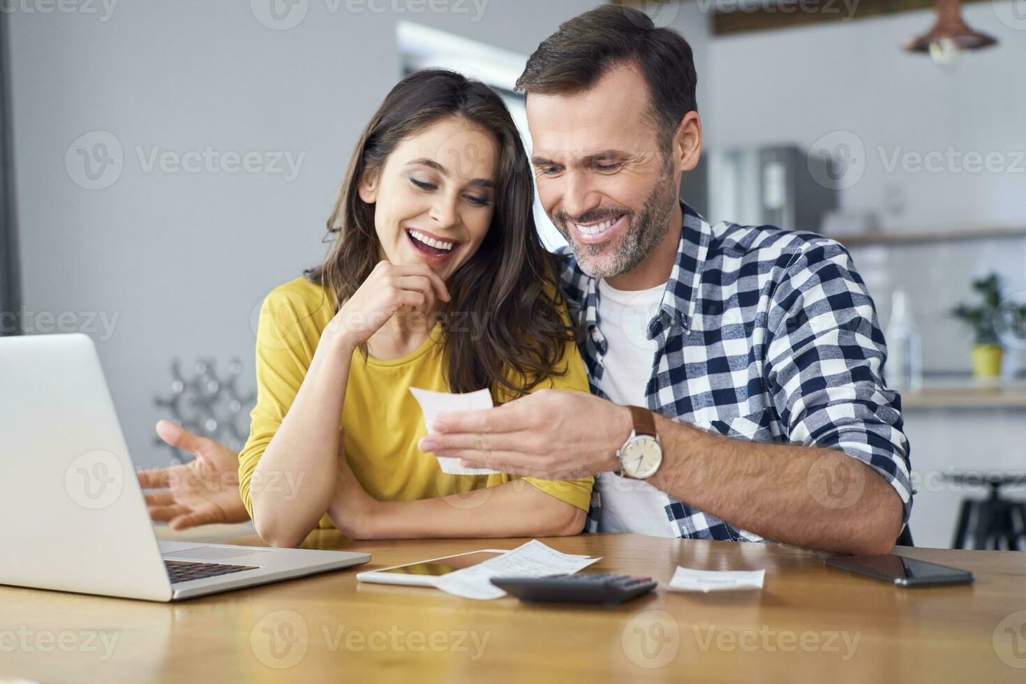 Couple sitting at dining table, using laptop, checking bills photo
