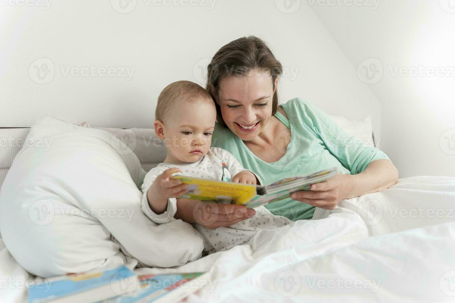 Mother and baby in bed reading picture book photo