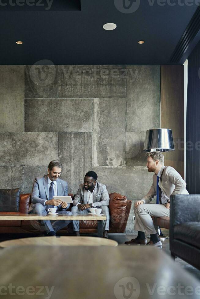 Three businessmen sitting in hotel lobby with tablet photo