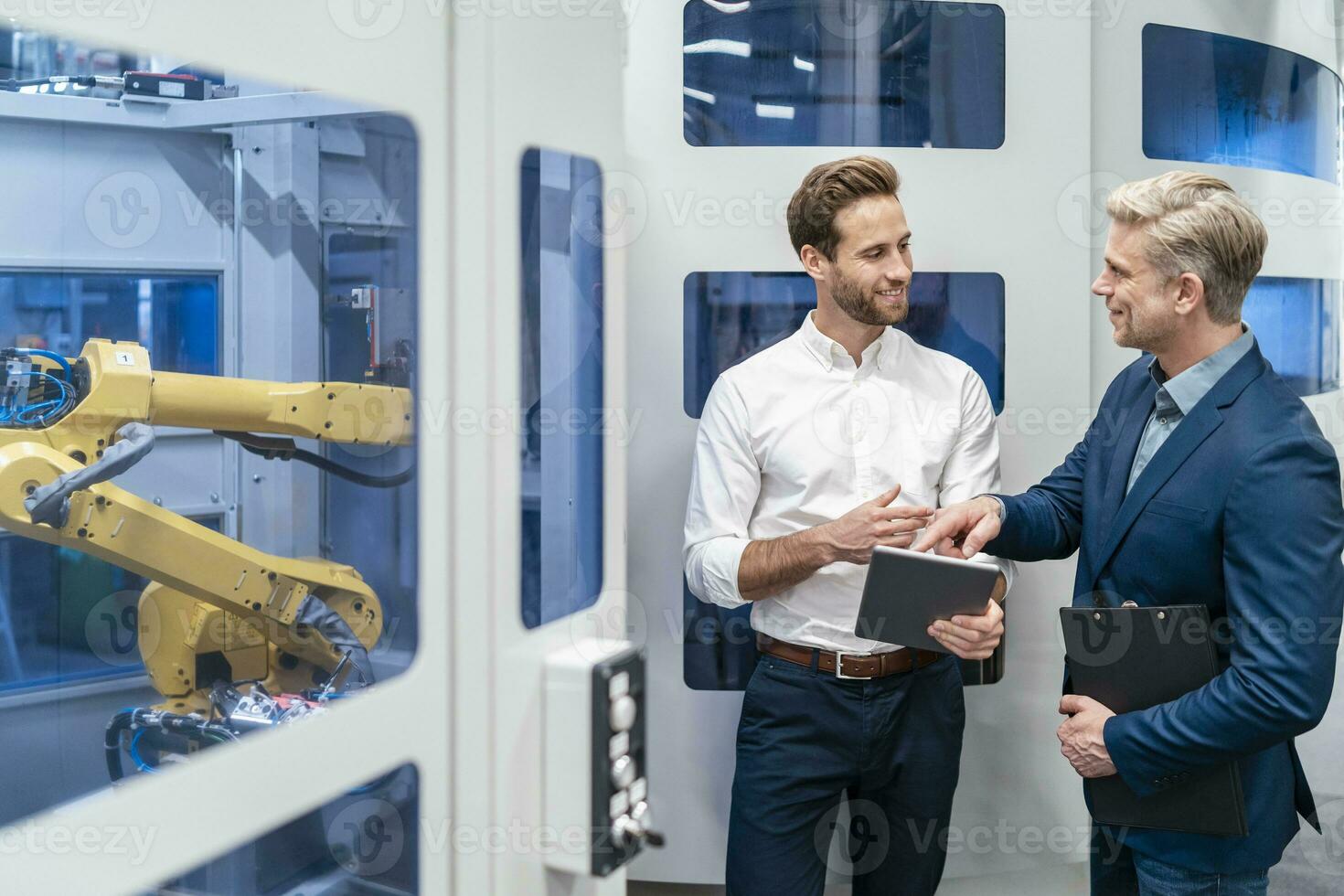 Two businessmen talking at robot in a modern factory photo
