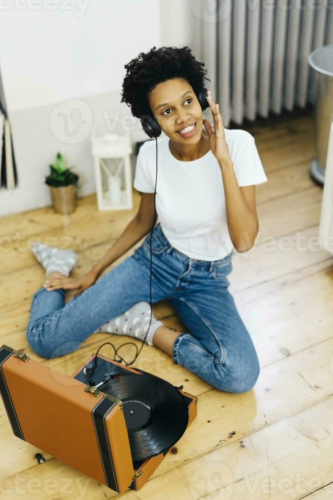 Young woman sitting on grounf listening music from record player, using headphones photo