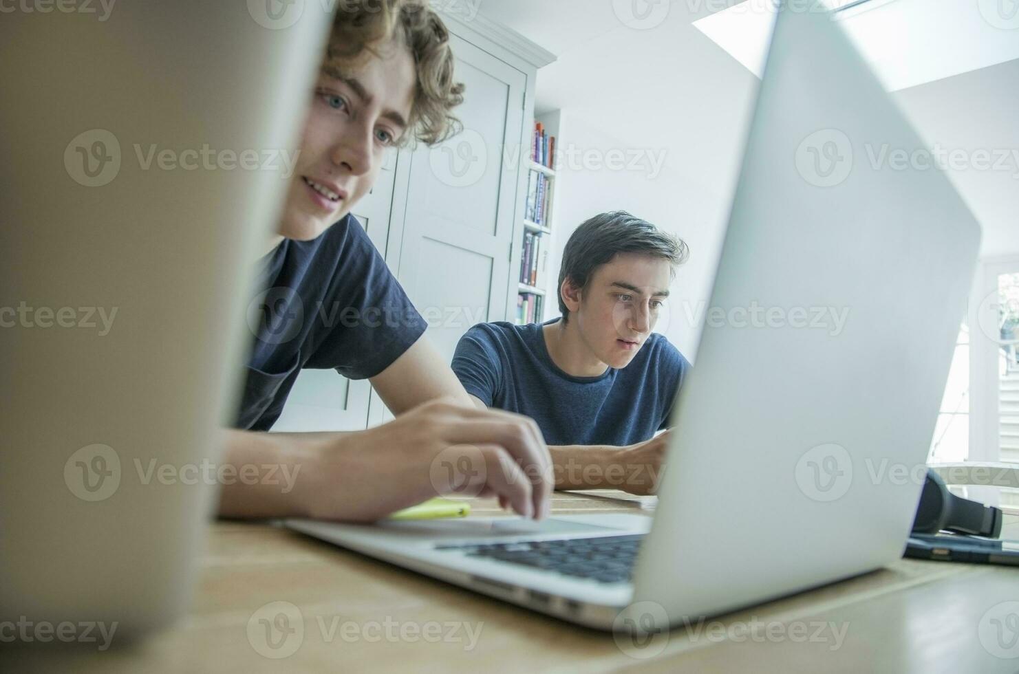 dos Adolescente Niños utilizando ordenador portátil y tableta en mesa a hogar foto