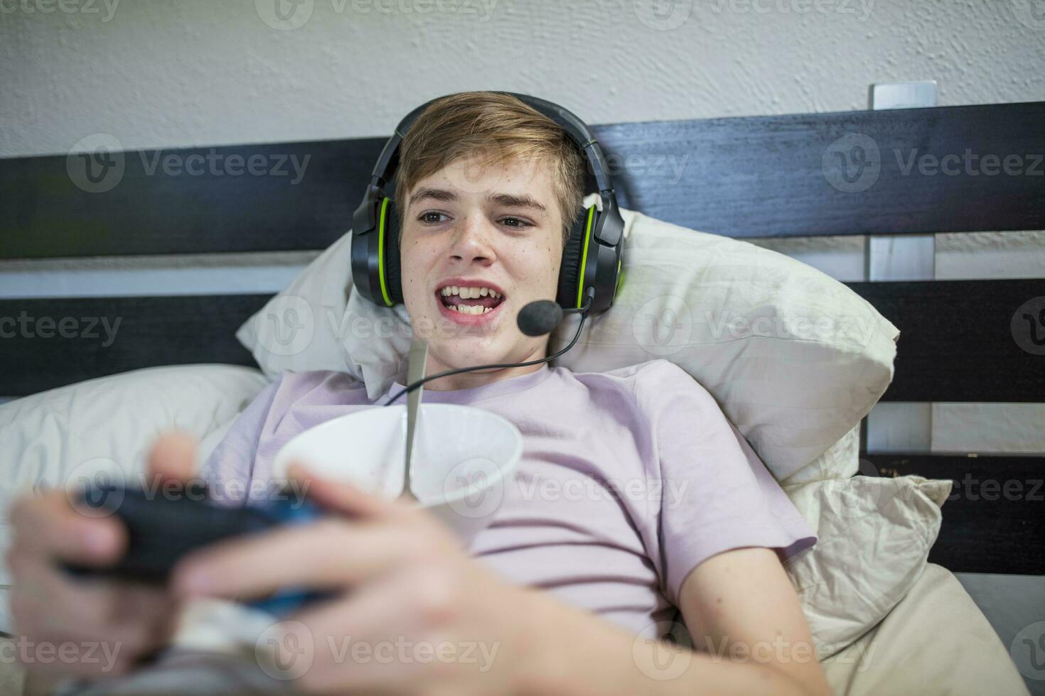 Boy lying in bed playing video game photo