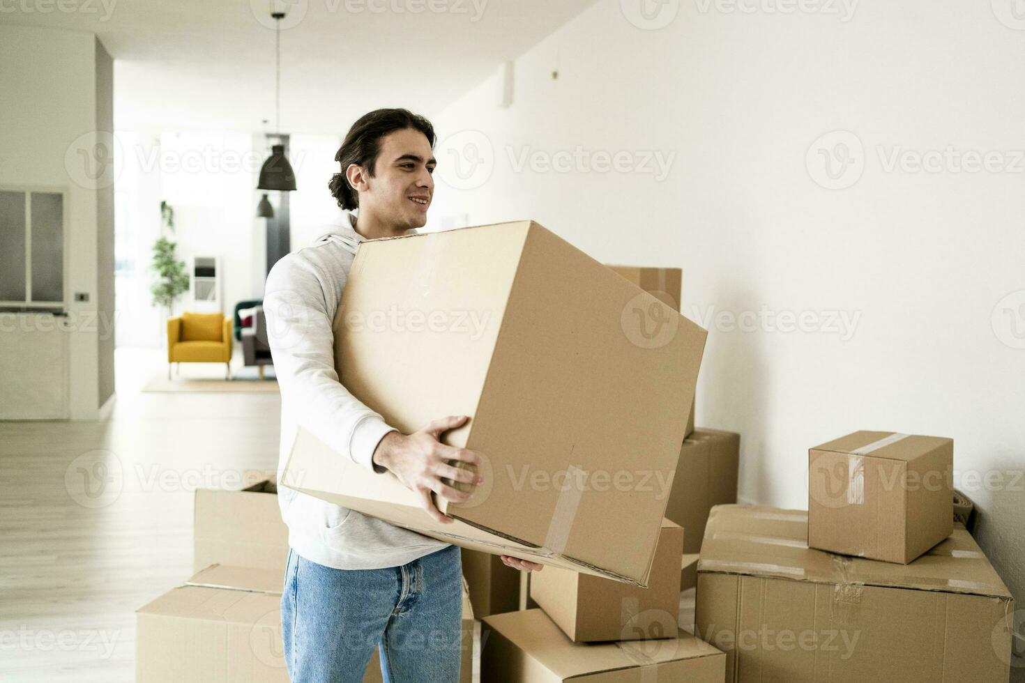 Smiling young man carrying cardboard box while moving in new apartment photo