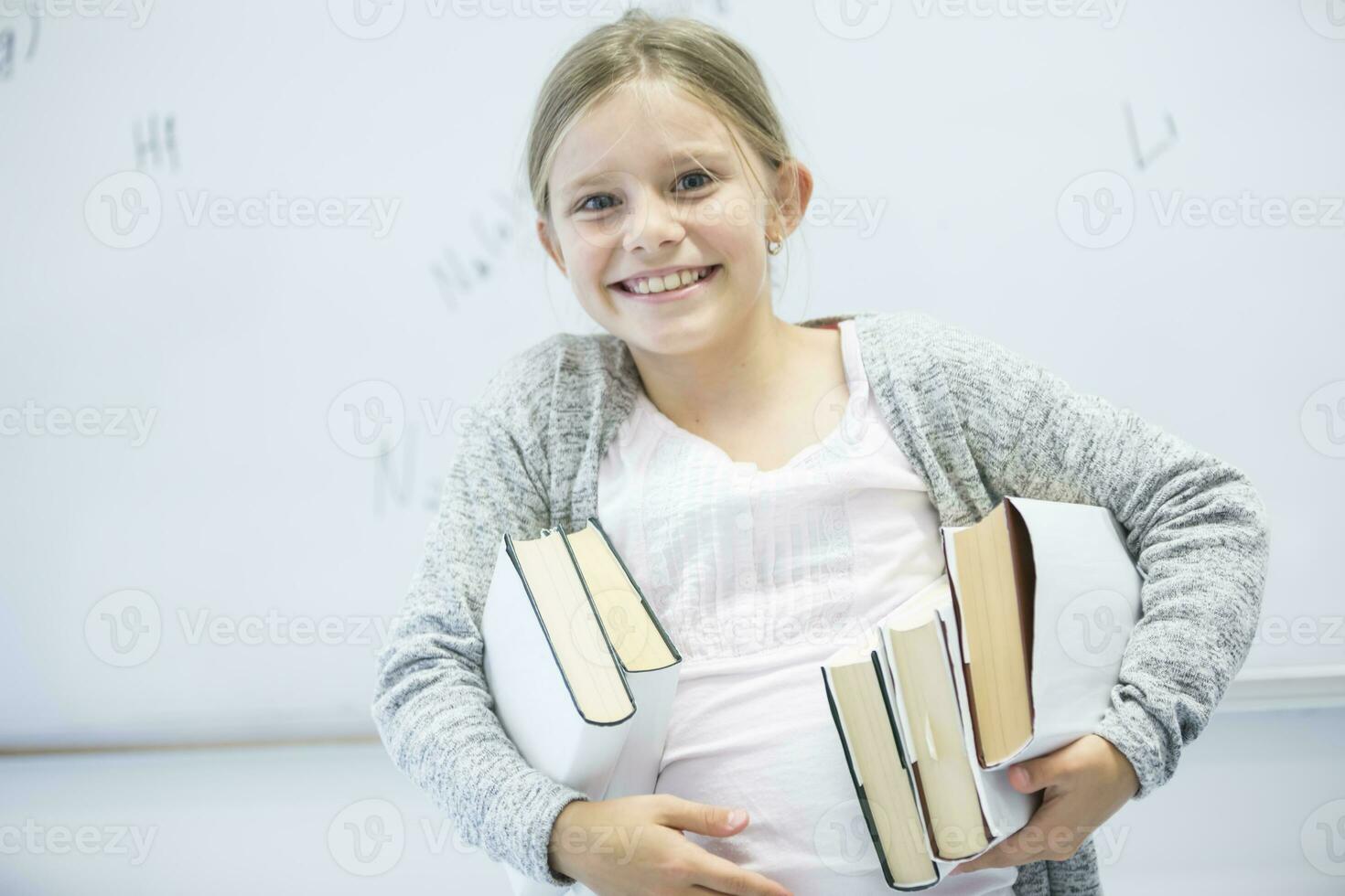 Portrait of happy schoolgirl carrying books in class photo
