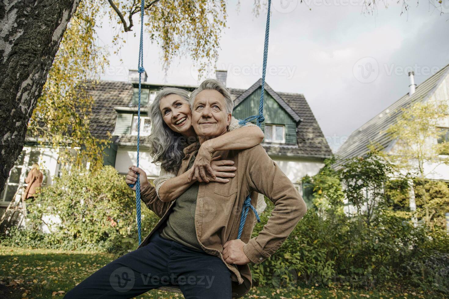 Happy woman embracing senior man on a swing in garden photo