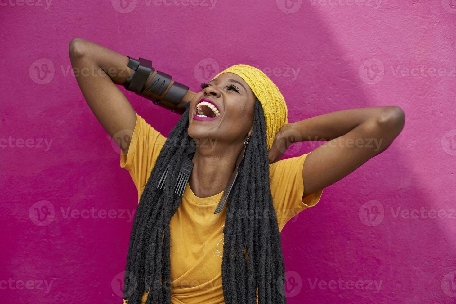 Portrait of woman with long dreadlocks laughing in front of a pink wall photo