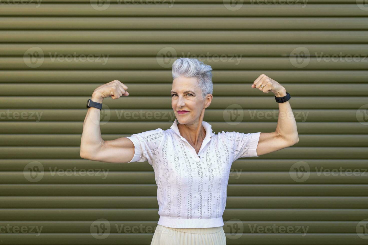 Senior woman flexing muscles while standing against shutter photo