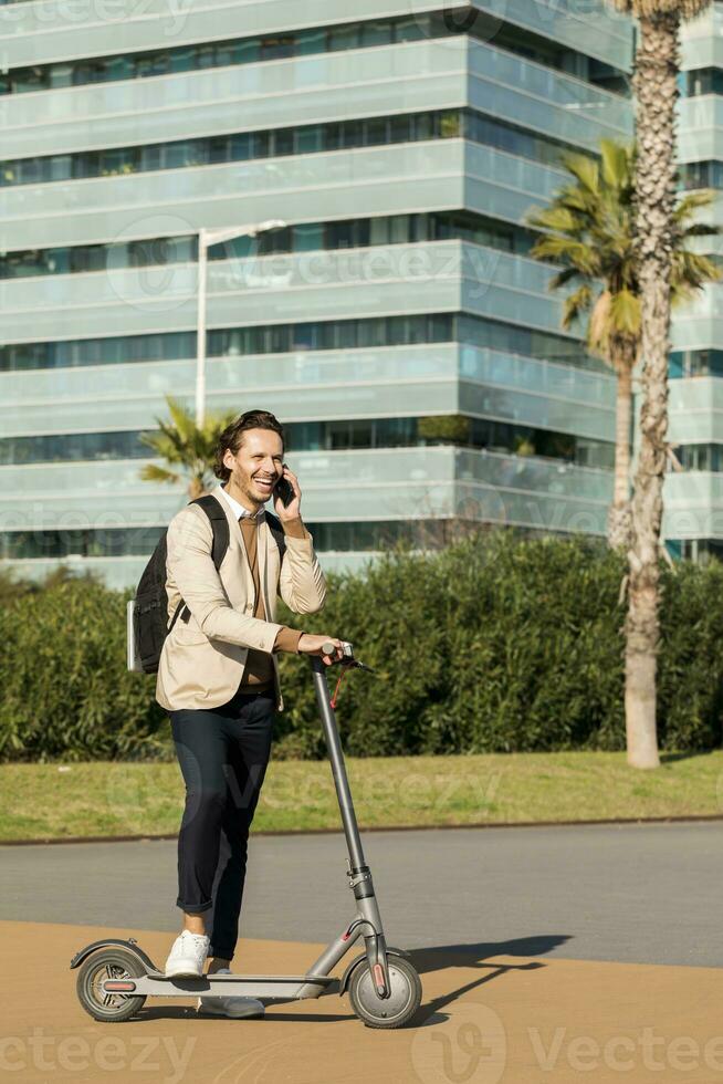 Laughing man on the phone with backpack and E-Scooter in the city photo