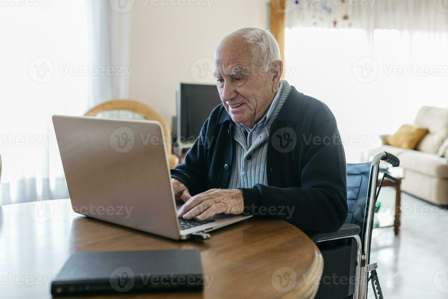 Portrait of content senior man in wheelchair using laptop at home photo