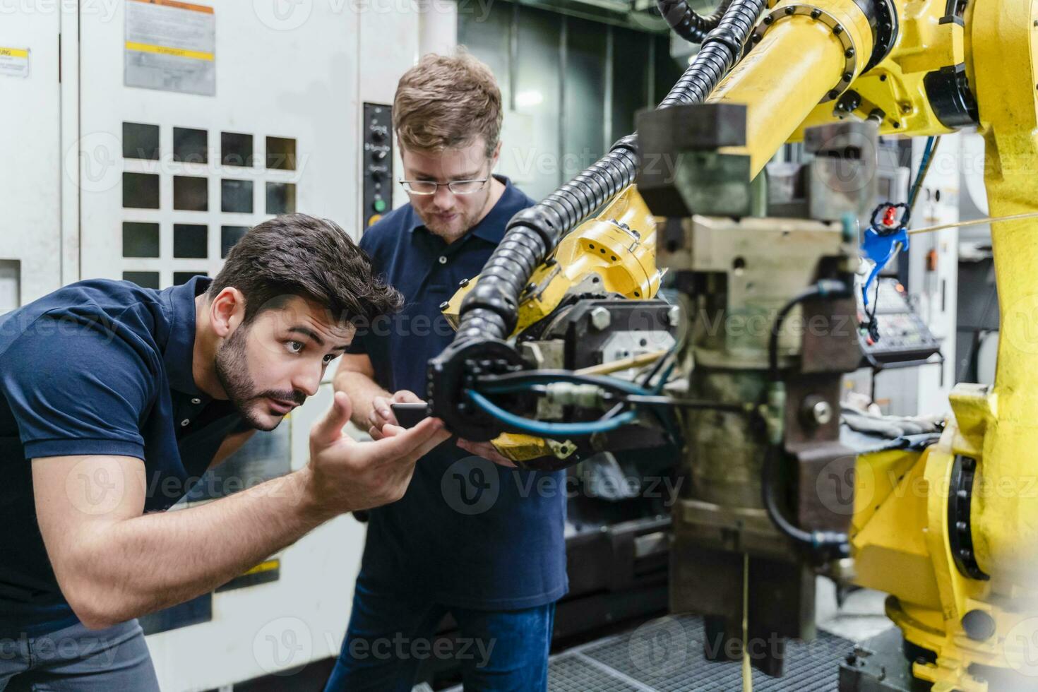 Male coworkers examining robotic arm while standing in manufacturing factory photo