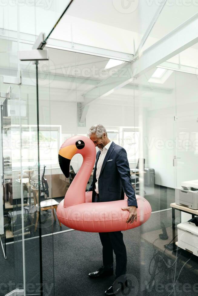 Happy businessman in office with inflatable flamingo photo