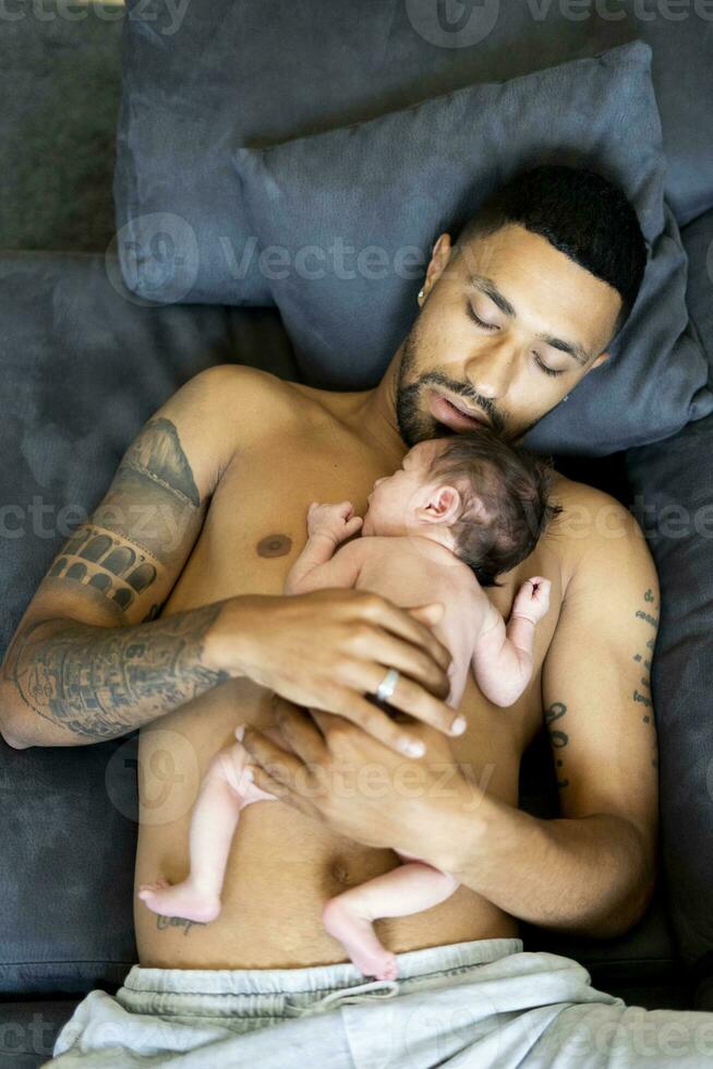 Father lying on couch with nude newborn baby photo