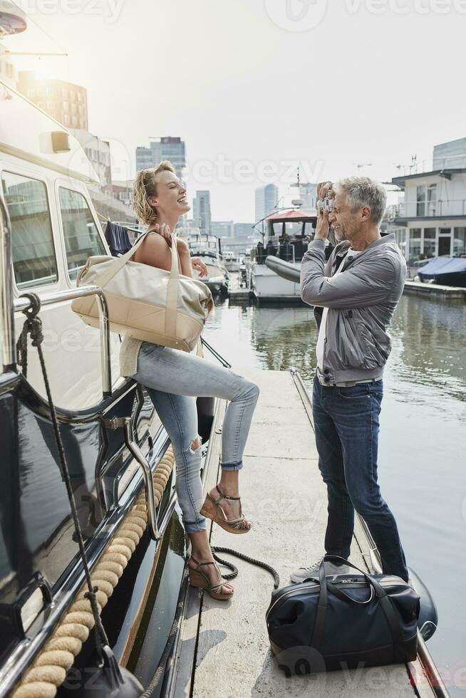 más viejo hombre tomando imagen de joven mujer en embarcadero siguiente a yate foto