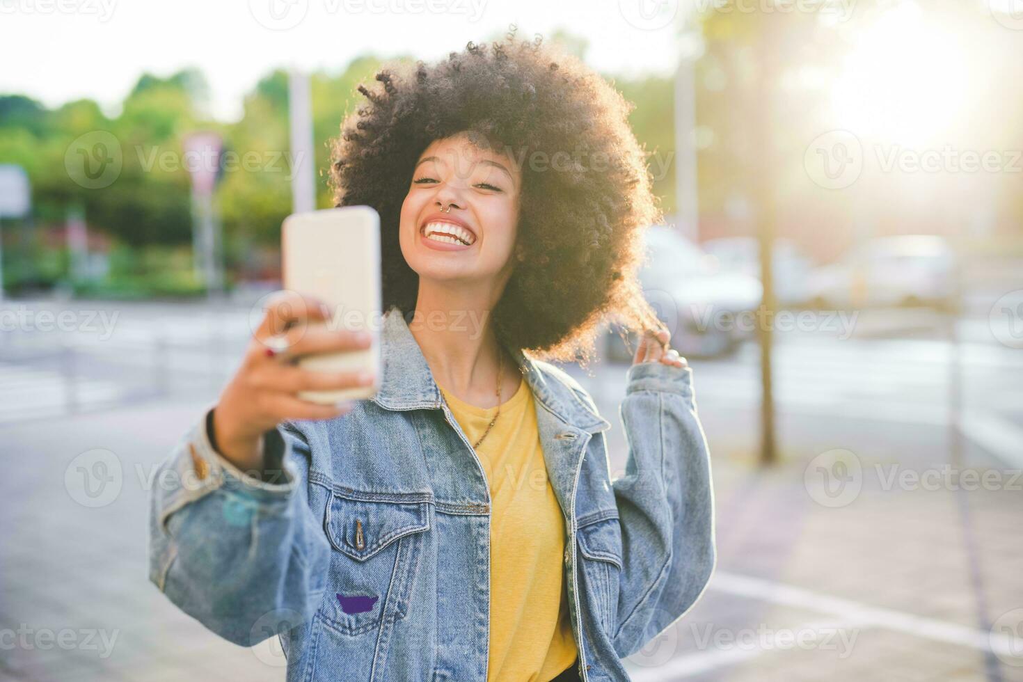 contento joven mujer con afro peinado tomando un selfie en el ciudad foto