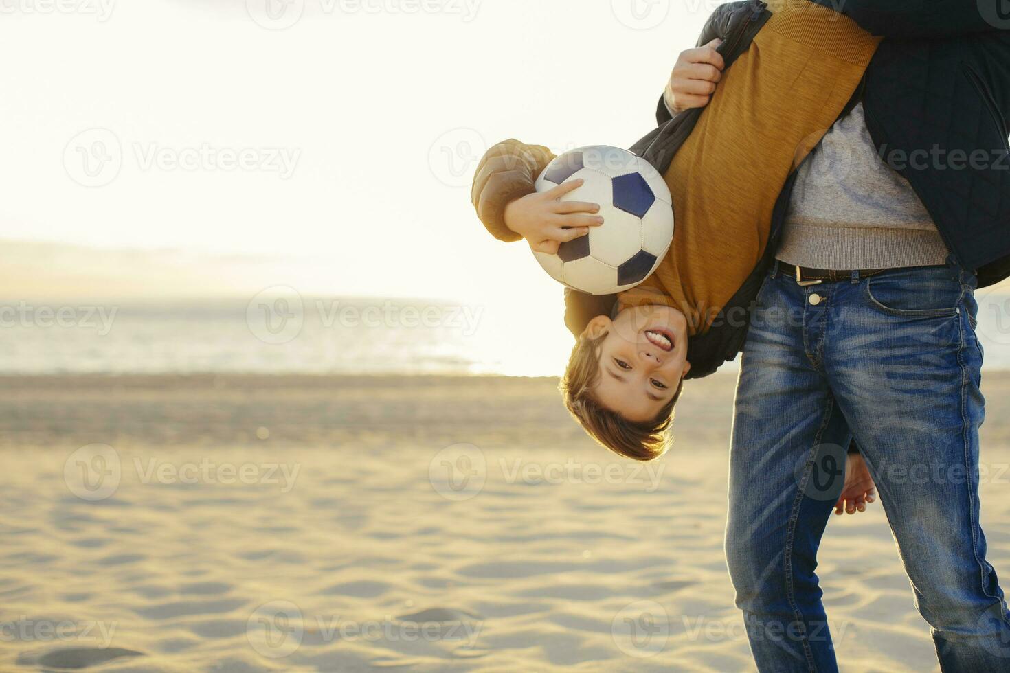 Father holding son with football upside down on the beach at sunset photo