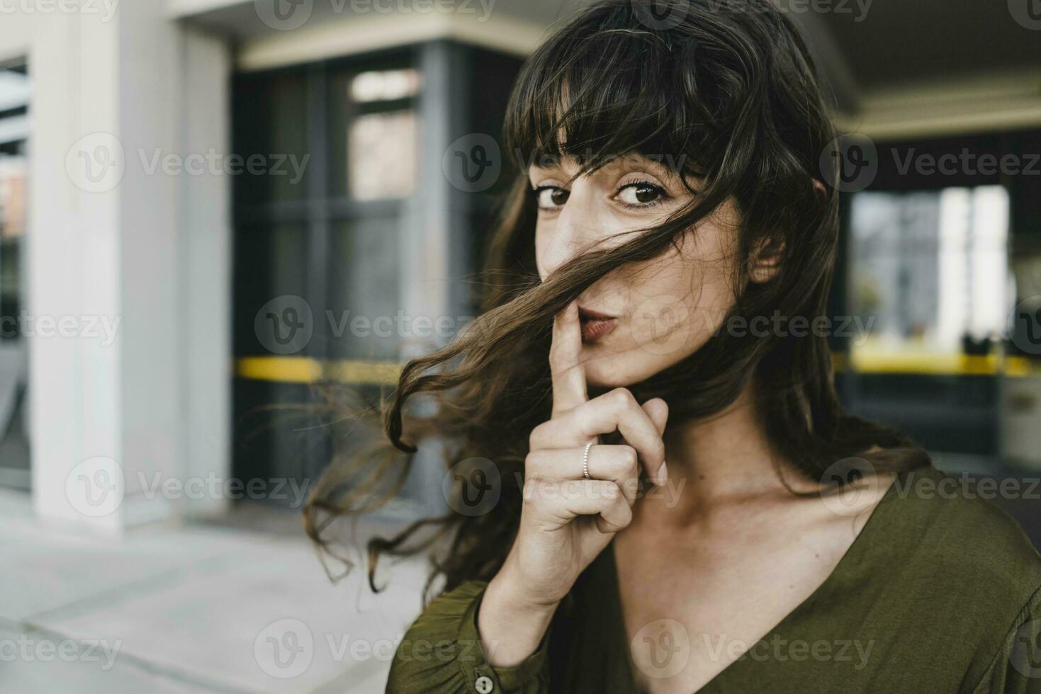 Portrait of smiling brunette woman, finger on mouth photo