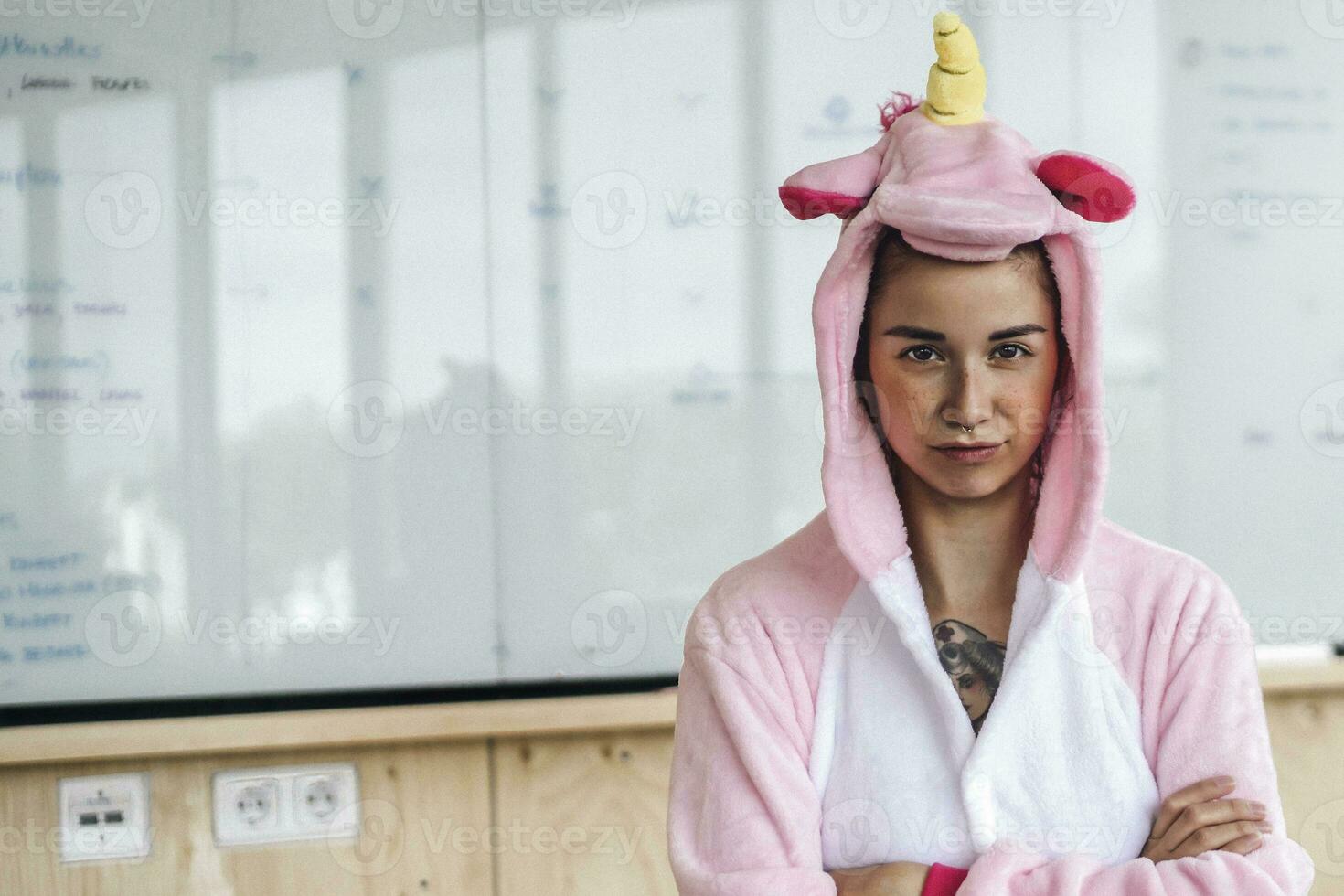 Woman wearing unicorn onesie, standing in front of whiteboard, looking stubborn photo