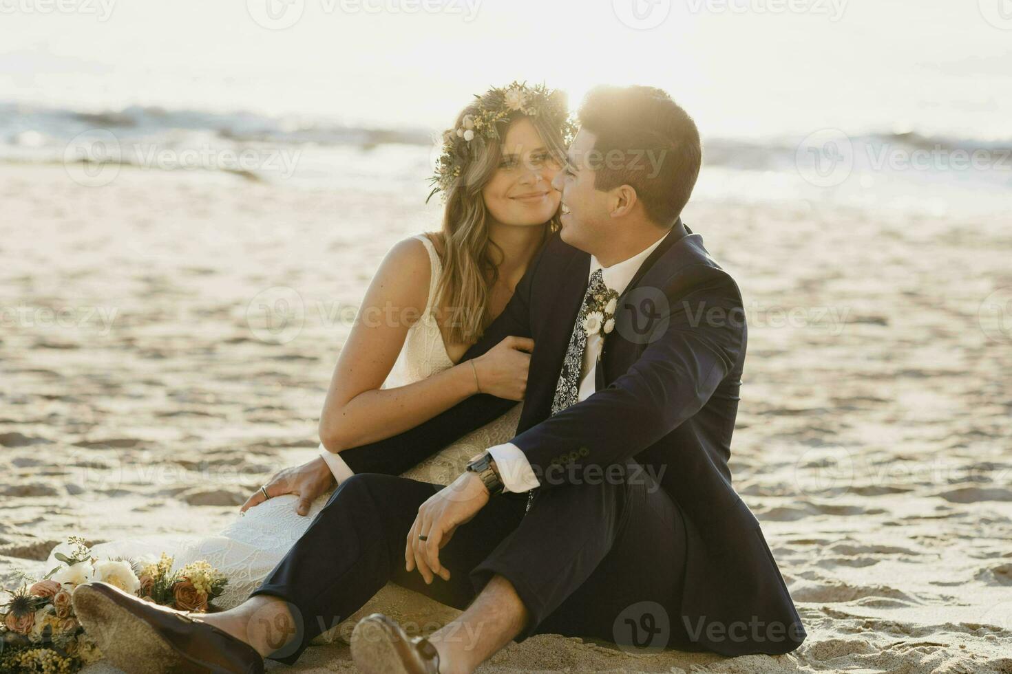 Happy bridal couple sitting at the beach photo