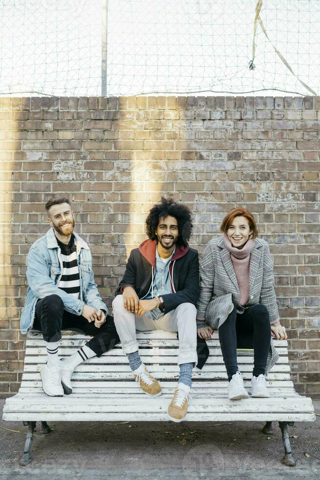 Portrait of three happy friends sitting on a bench in front of a brick wall photo