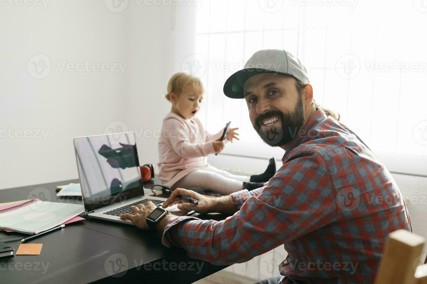 padre trabajando desde hogar, utilizando ordenador portátil con su gatillo sentado en el escritorio, jugando foto