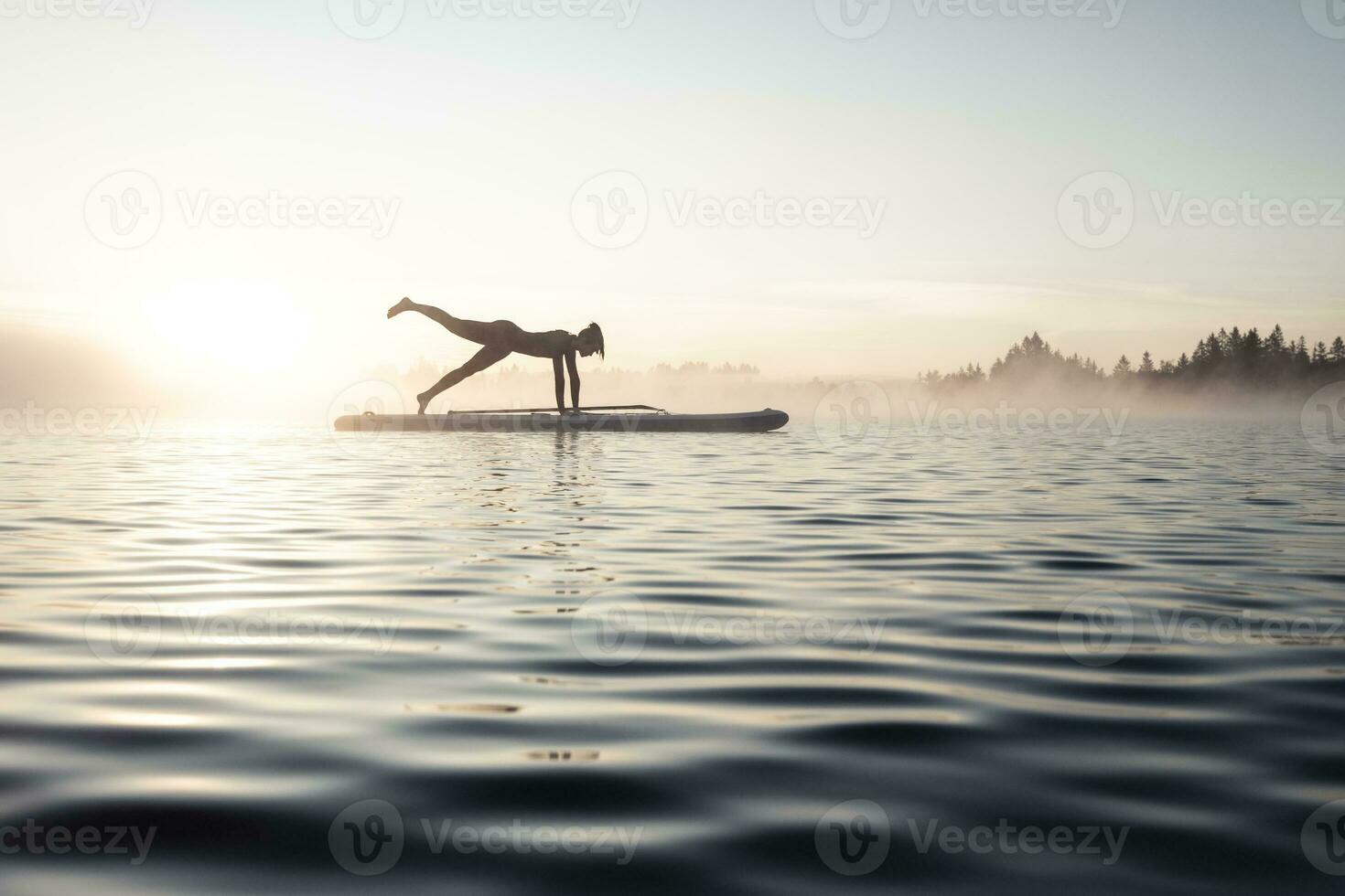 Woman practicing paddle board yoga on lake Kirchsee in the morning, Bad Toelz, Bavaria, Germany photo