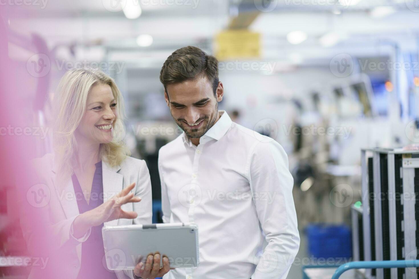 Smiling businesswoman discussing with young male colleague in illuminated factory photo