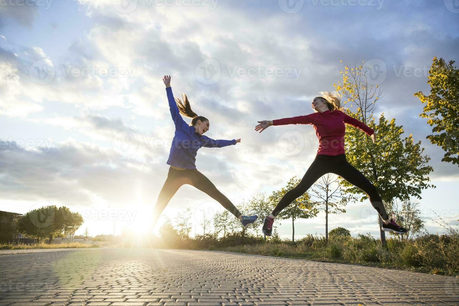 Young women having fun and jumping in park, against morning sun photo