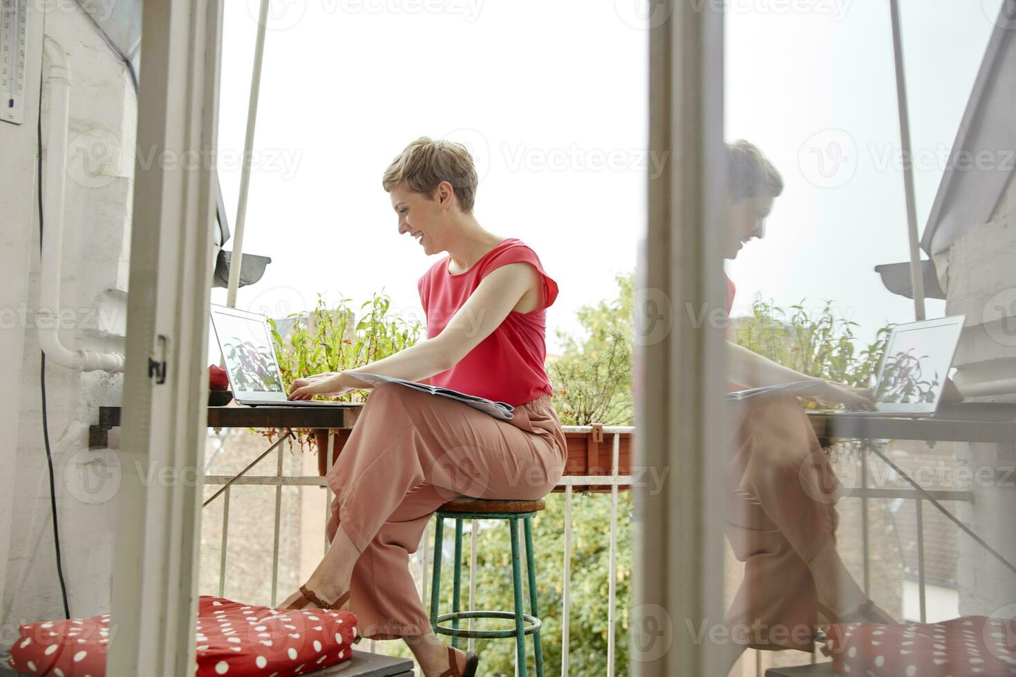 Happy woman sitting on balcony at home with laptop and map photo