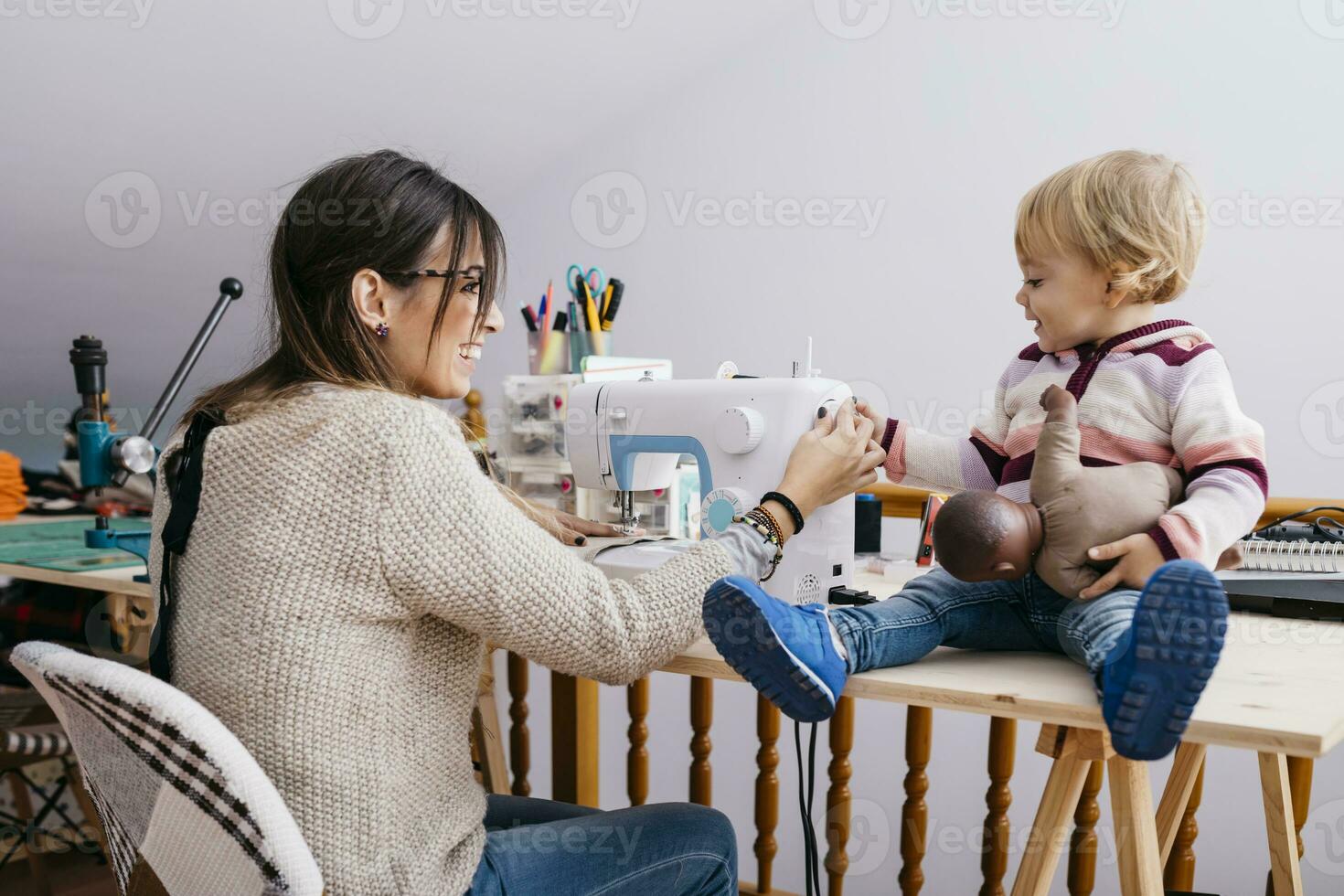 Happy mother with little daughter at home using sewing machine photo