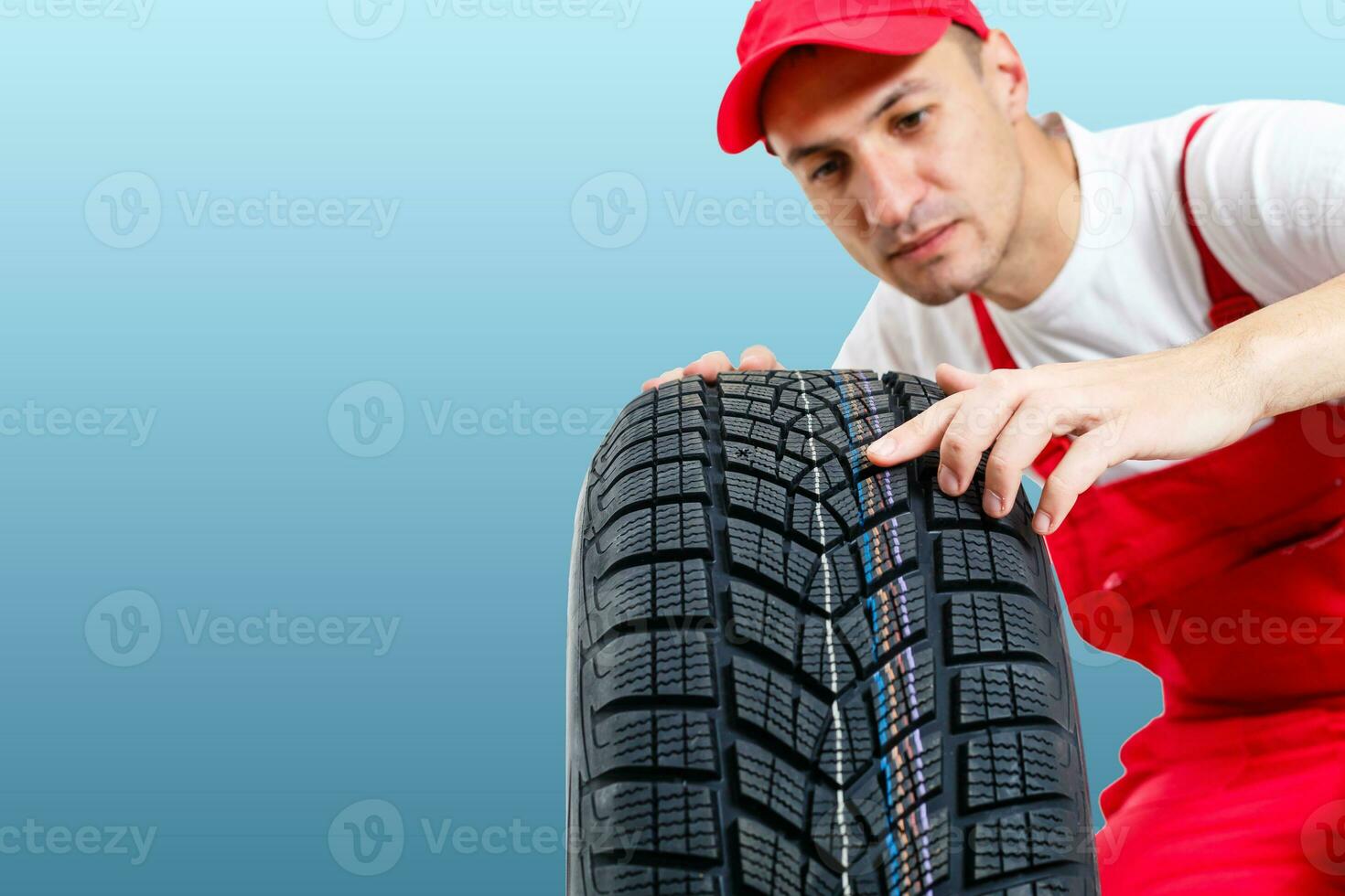 car mechanic carrying tire on blue background. happy man smiling amd looking into camera photo