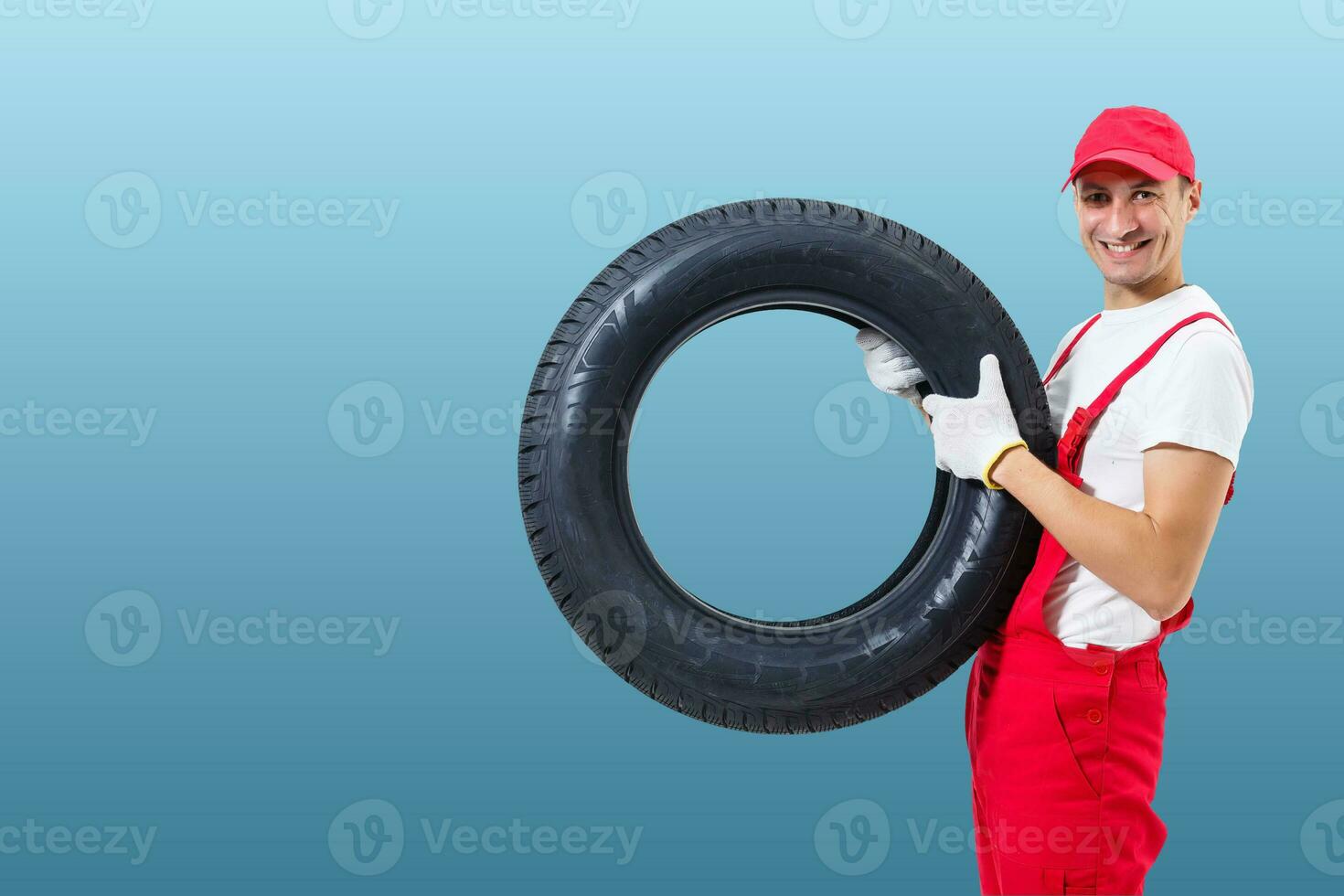car mechanic carrying tire on blue background. happy man smiling amd looking into camera photo