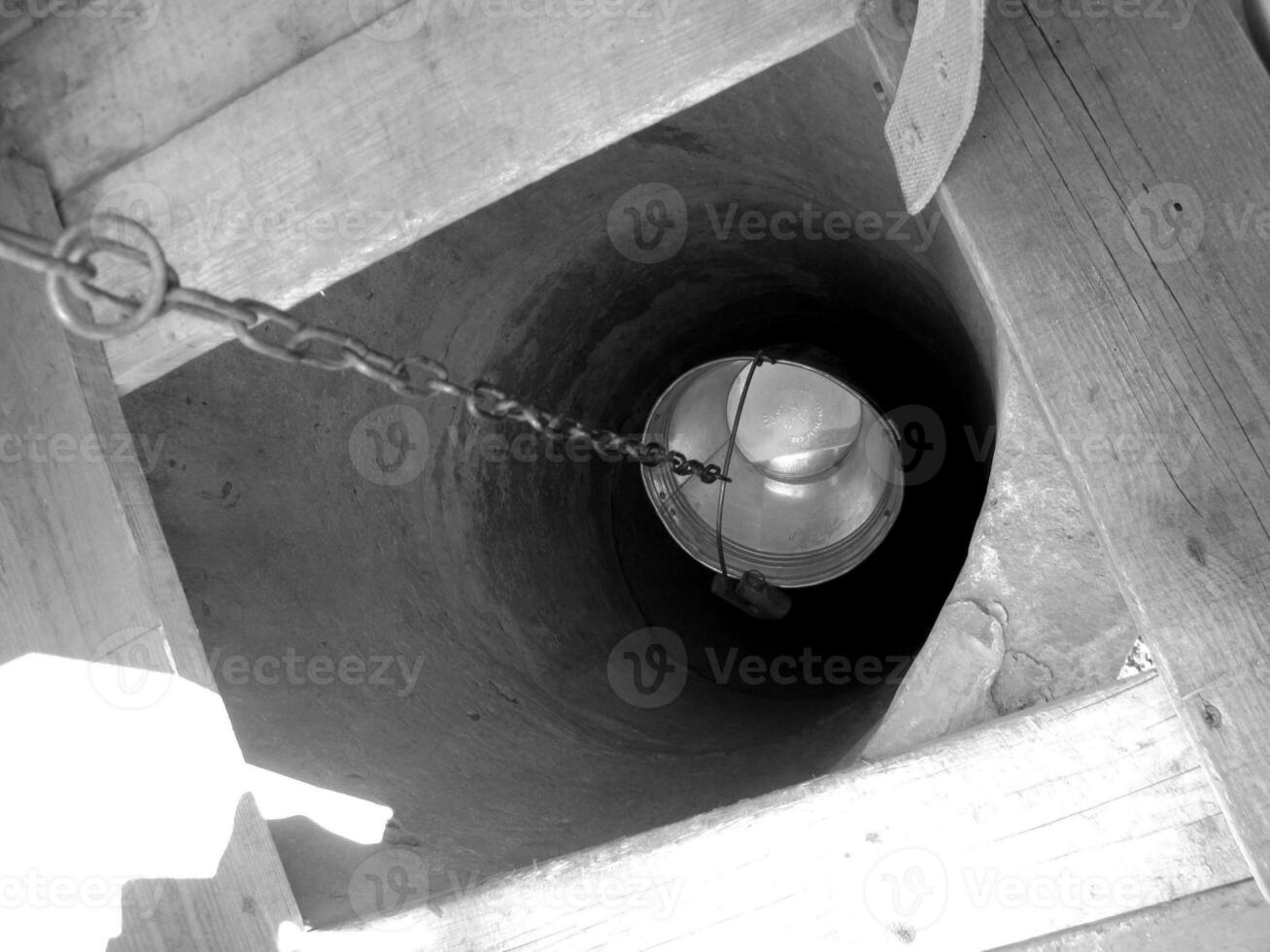 Old well with iron bucket on long forged chain for clean drinking water photo