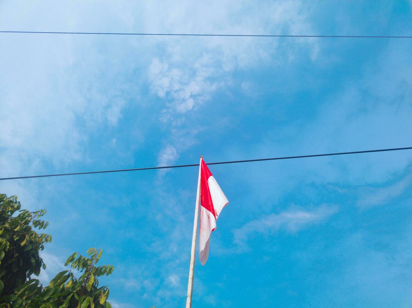 red and white flag of Indonesia against the sky and power lines in the background photo